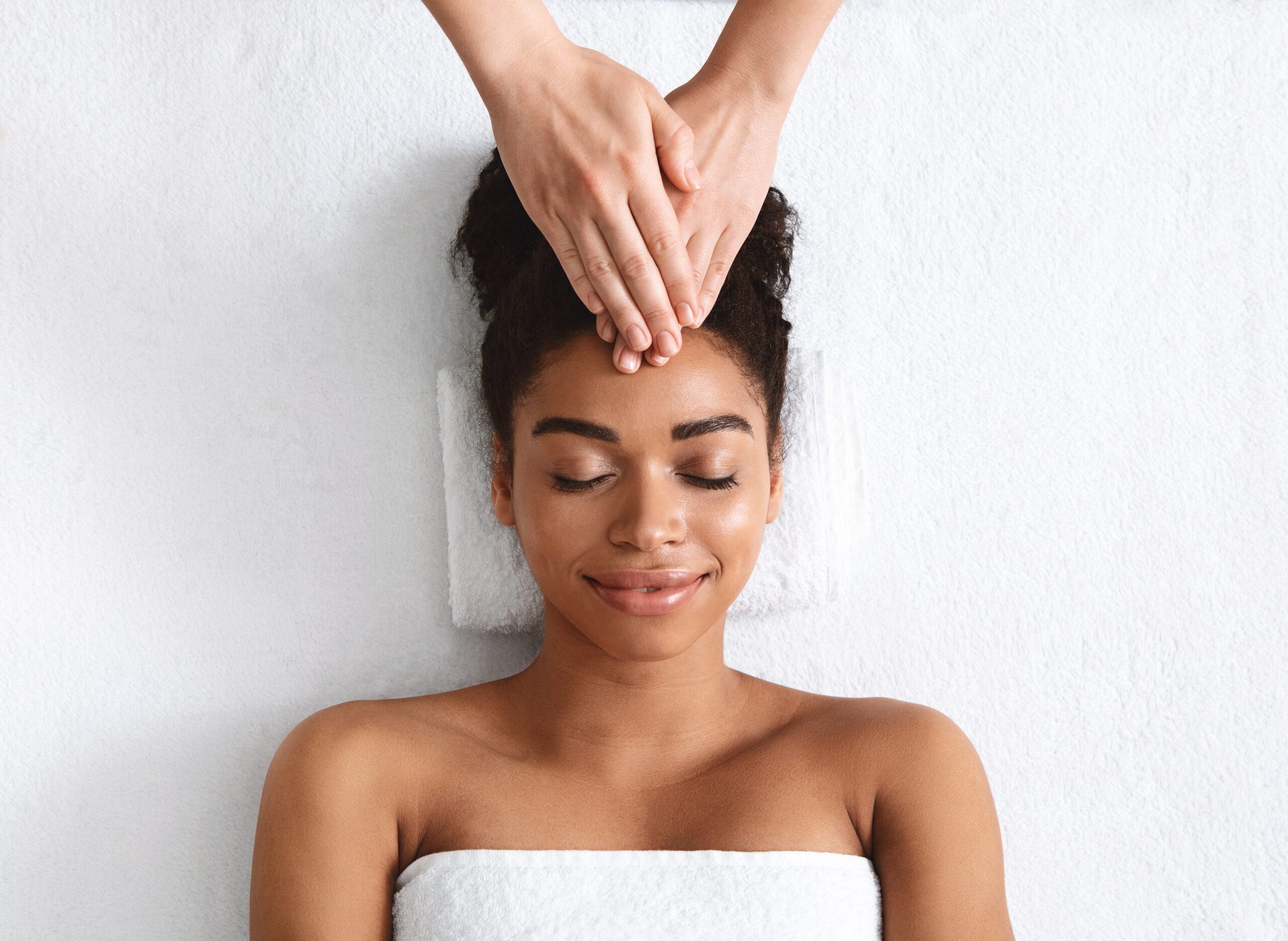 Therapist rubbing black woman forehead at spa
